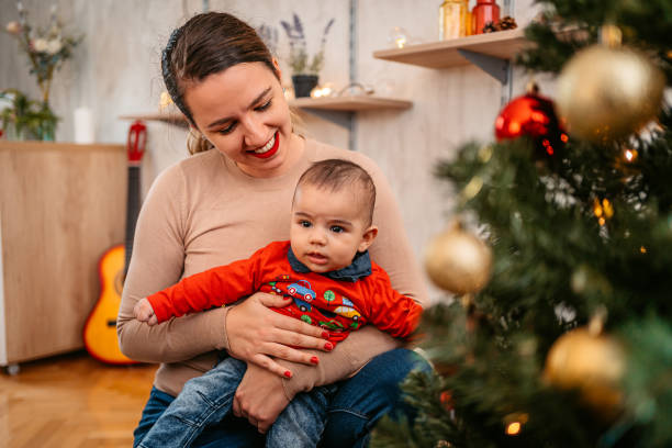 istock Mother holding baby boy playing next to Christmas tree 1356194987