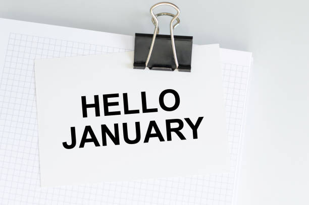 istock HELLO JANUARY text on a white card that is clipped to a white notepad on the table. 1356197602