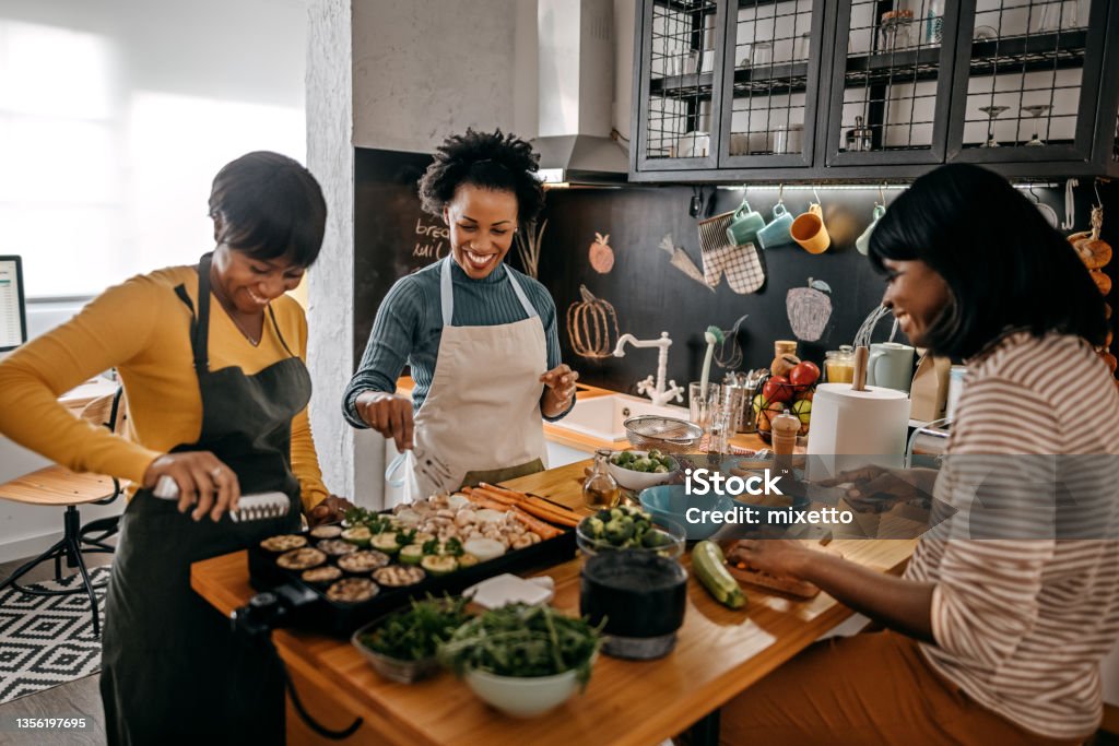 Three female friends cooking food in kitchen Three happy female friends preparing food in domestic kitchen for thanksgiving celebration Thanksgiving - Holiday Stock Photo