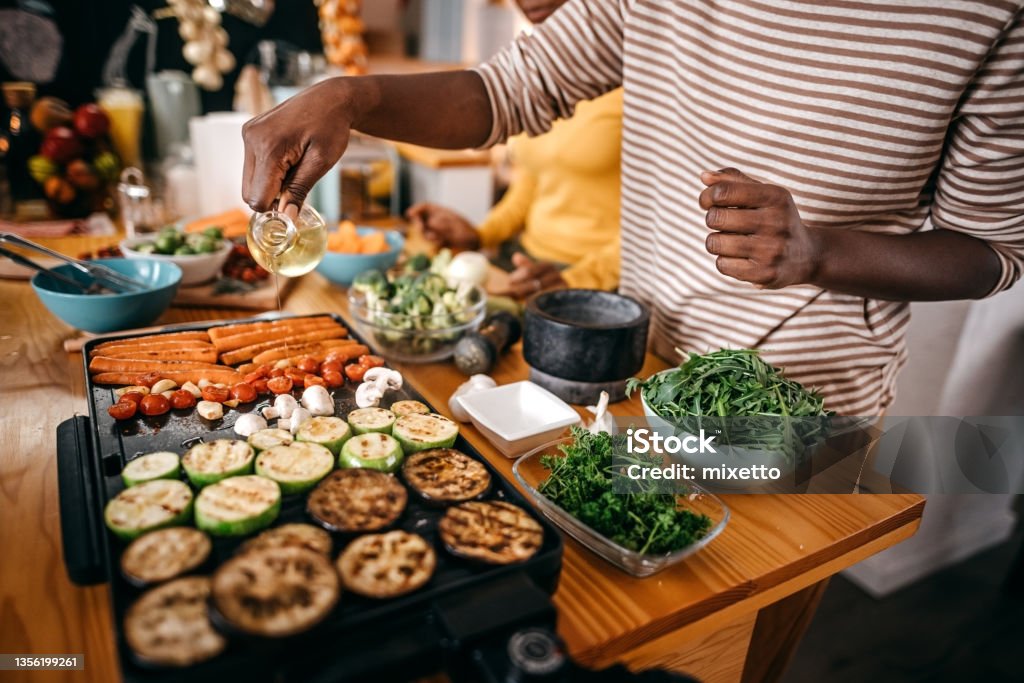 Woman pouring cooking oil on barbecue grill while preparing food Woman pouring cooking oil on electrical barbecue grill while roasting vegetables for thankgiving celebration Grilled Stock Photo