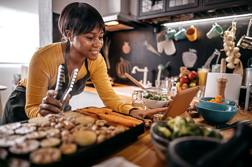 Woman watching recipe in digital tablet while grilling food on electrical barbecue at domestic kitchen