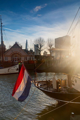 Rotterdam, Netherlands - February 24, 2021; Dutch flag on a boat in Rotterdam's Veerhaven and modern office buildings on the Kop van Zuid in the background