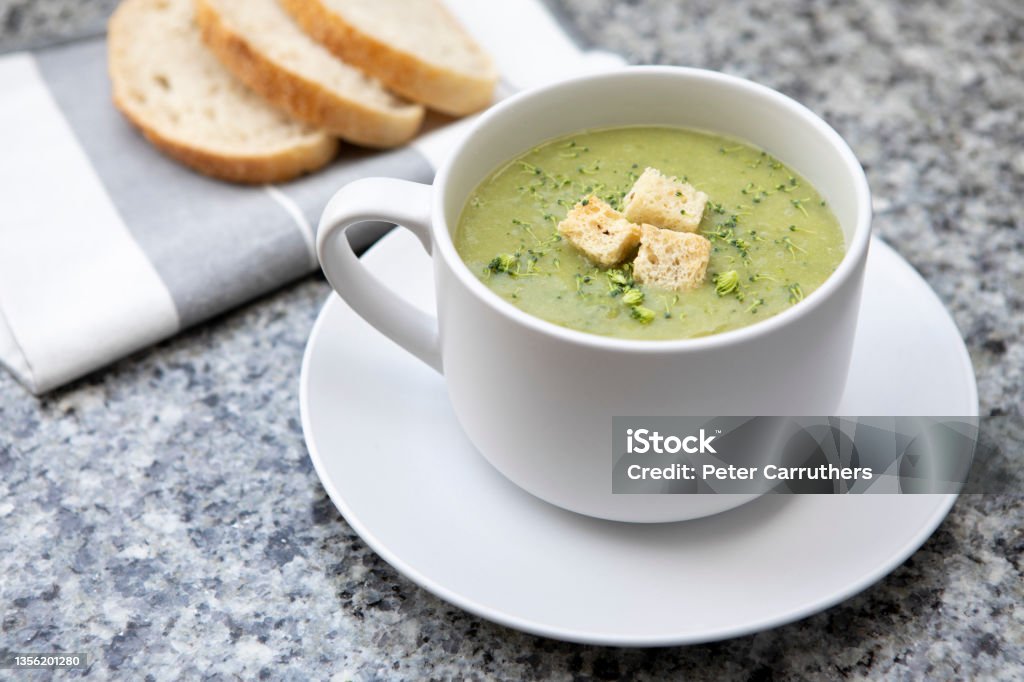 Broccoli and Stilton soup with croutons in a giant cup and saucer, with slices of sourdough bread on a napkin, on a granite surface Healthy meal of hot winter soup with slices of sourdough bread Broccoli Stock Photo
