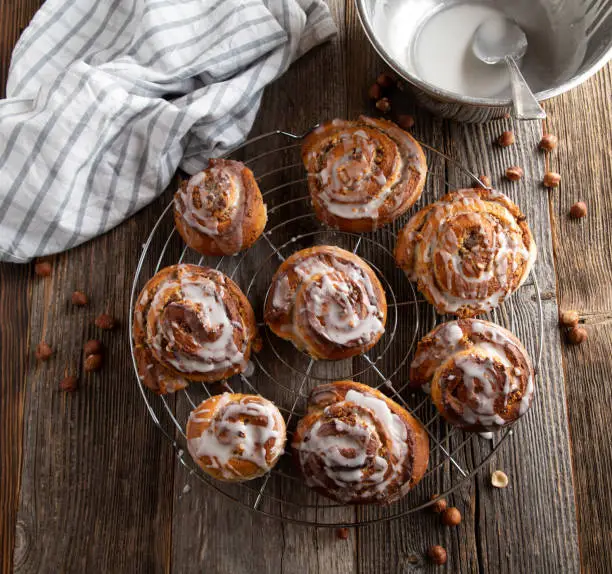 Fresh and homemade baked cinnmon rolls filled with hazelnuts and served on a cooling rack on wooden table. Closeup and overhead view