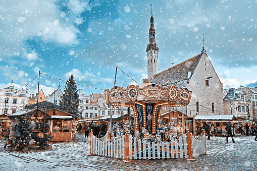 View of old Tallinn central square during Christmas market. Vintage carousel, Christmas tree and kiosks illuminated with Xmas light and walking crowd