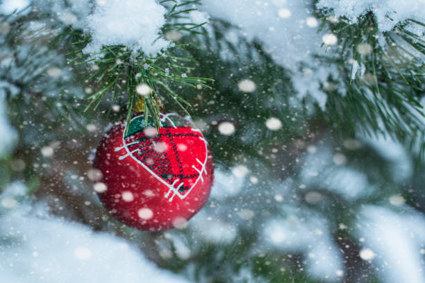 A red bauble with a heart hung on a snow-covered Christmas tree twig stock photo