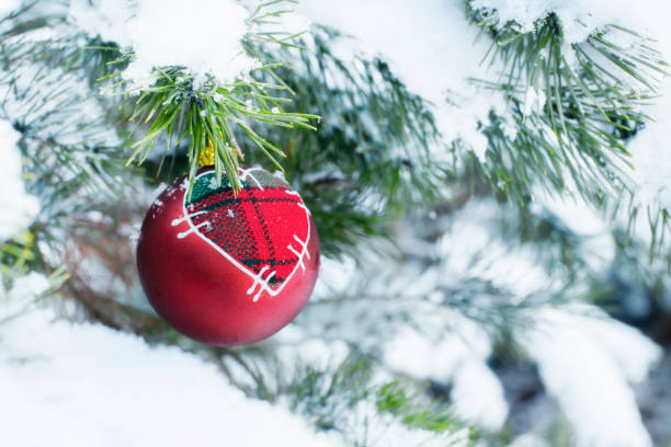 A red bauble with a heart hung on a snow-covered Christmas tree twig stock photo