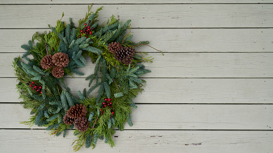 Natural evergreen holiday wreath with pine cones and winterberries on old rustic wood siding with peeling paint and copy space