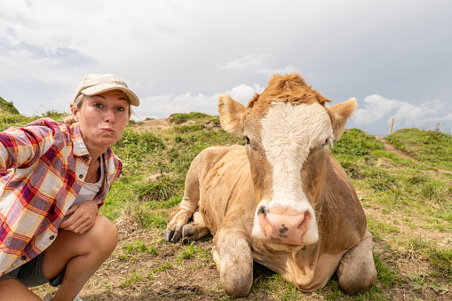 She smiles at the camera,  cattle cow beside her\nAppenzelerland canton, Switzerland