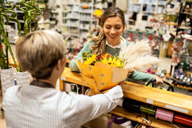 Florist selling a beautiful flower bouquet to a young woman customer Senior florist selling a flower bouquet to a young customer. sunflower star stock pictures, royalty-free photos & images