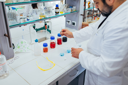 Using a pipette, the chemist precisely injects the liquid solution into a laboratory glassware and monitors its reaction.