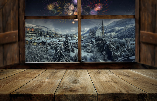 Wooden table and window with blurred christmas scene and fireworks at new year