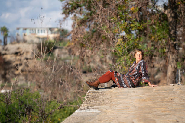 istock Mature woman sitting on stone bridge and looking at camera. 1356210807