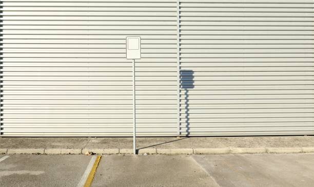 White empty sign on a pole in front of a white aluminium cladding wall. Concrete sidewalk and road side. Background for copy space
