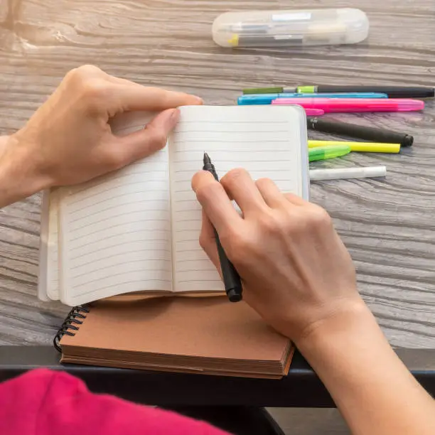 Woman hands taking notes in open lined notebook with black liner pen. Education.