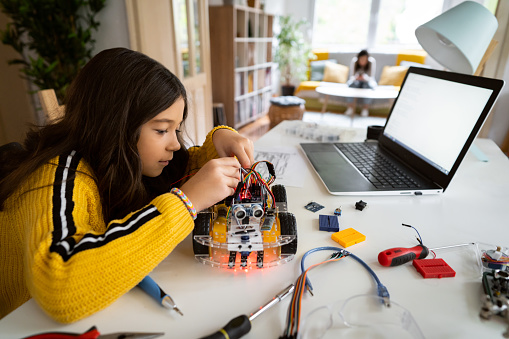 Curious and smart schoolgirl, repairing her prototype of an autonomous self-driven robotic car, for a school science project, with a screwdriver