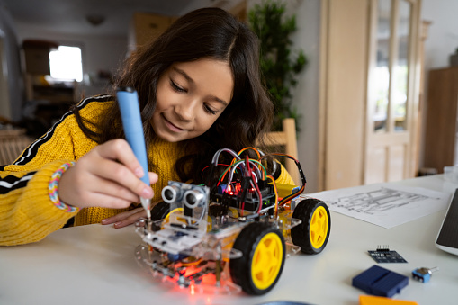 With a screwdriver, smart and dedicated schoolgirl, adjusting and repair her prototype of an autonomous self-driven robotic car with sensors