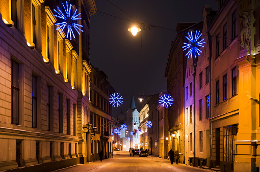 Panorama of a winter evening in the city, illuminated by evening street lights, before Christmas. Snowy streets, snowflakes. Riga, Latvia.