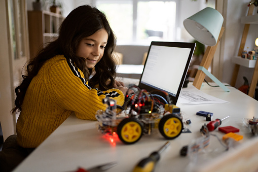 Via open-source hardware and software platform, dedicated and smart Caucasian school girl, testing her prototype of an autonomous self-driven robotic car