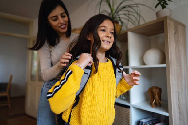 istock Schoolgirl, ready to go to school while her mother adjusting her backpack 1356216201