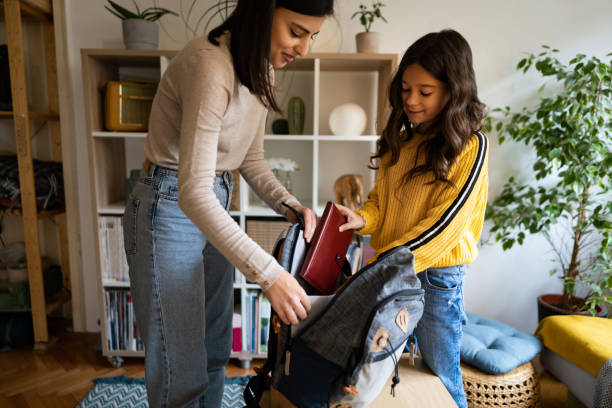 Schoolgirl, packing her backpack with school supplies with a help of her mother stock photo