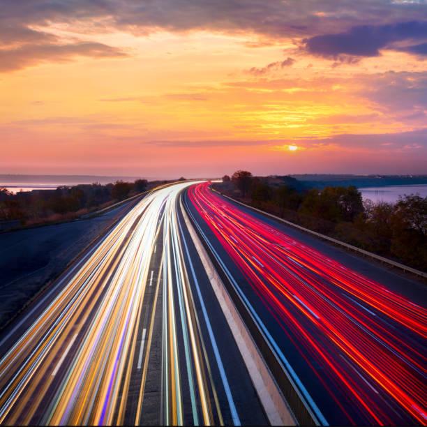 Trails  of cars lights on the asphalt road. Sunset sundown time. Drive forward! Transport creative background. Long exposure, motion and blur. Trails  of cars lights on the asphalt road. Sunset sundown time with clouds and sun. Drive forward! Transport creative background. Long exposure, motion and blur."n Long Time Exposure stock pictures, royalty-free photos & images