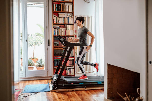 Woman training on treadmill at home Woman getting fit and doing home training in the living room during lockdown of corona virus crises. treadmill stock pictures, royalty-free photos & images