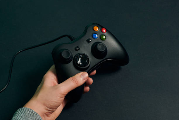 istock Hand of a man holding a video console controller on a black background 1356220027