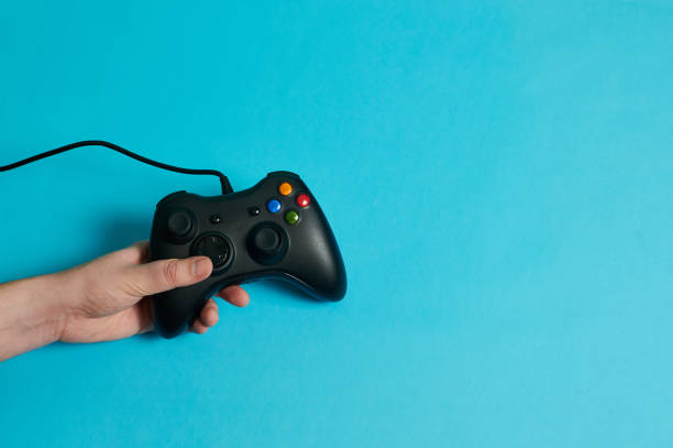 istock Hand of a man holding a video console controller on a blue background 1356220038