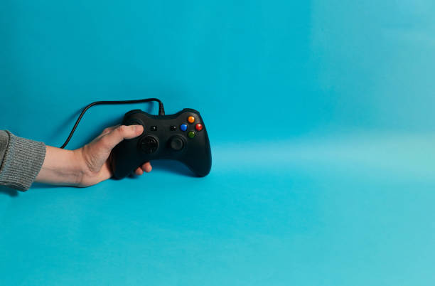 istock Hand of a man holding a video console controller on a blue background 1356220109