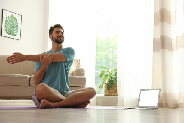 istock Man practicing yoga while watching online class at home during coronavirus pandemic. Social distancing 1356221121