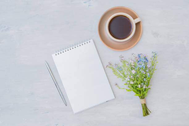 istock Flat lay composition with a mockup notebook, a cup of coffee and small blue flowers on a light background 1356221426