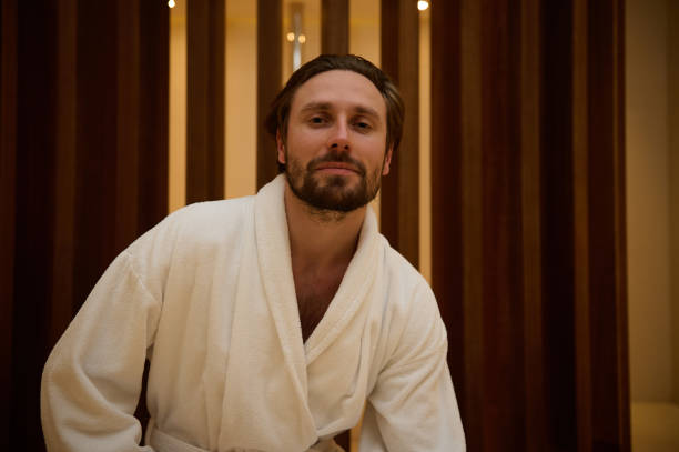 istock Attractive middle-aged man with a charming look and a slight unshaven, handsome macho in a white bathrobe stands in the lobby of a luxury spa centre, looking confidently and mysteriously at the camera 1356221703