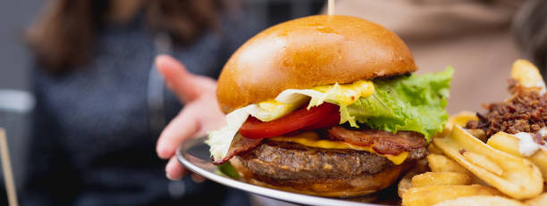 istock Horizontal banner or header bacon burger holden by unrecognizable female hands. 1356221755