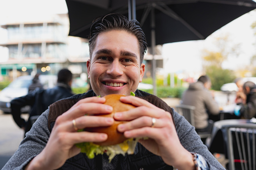 Portrait of latin hispanic man looking at camera smiling holding a hamburger.