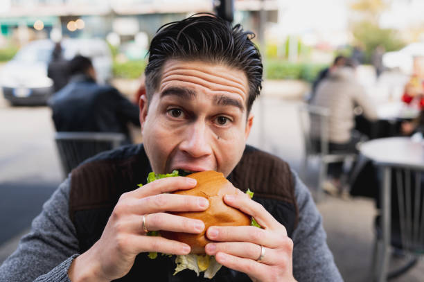 istock Close-up male biting a hamburger while looking at camera. 1356222607