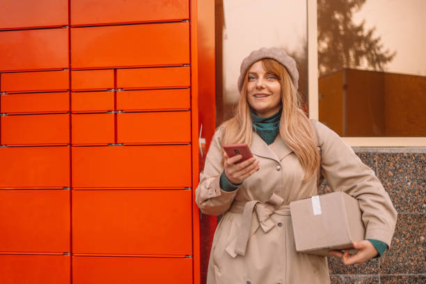 istock Pickup parcel. Young caucasian woman using automated self service post terminal machine or locker to deposit the parcel for storage 1356222665