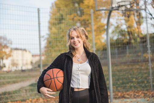 Attractive teenage girl with a basketball on outdoor court. Happy girl in casual clothing with a basketball on court.