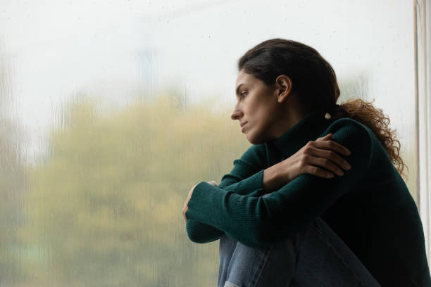 Lonely young latina female sit on windowsill watch rain outside Raindrops like tears. Sad lonely latina female sit on windowsill in melancholic mood watch rain outside feeling her heart broken. Pensive young woman hug herself suffer of unanswered love. Copy space grief stock pictures, royalty-free photos & images