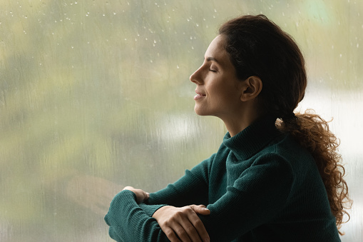 Serena mujer latina relájate por la ventana escucha el sonido de las gotas de lluvia photo