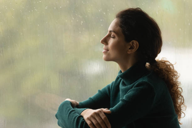 Serene latin woman relax by window listen sound of raindrops Music of rain. Side shot of serene latin woman relax by window with closed eyes listen sound of raindrops feel pleasure. Calm young lady enjoy breathing fresh ozonized air after rainstorm. Copy space. relief emotion stock pictures, royalty-free photos & images
