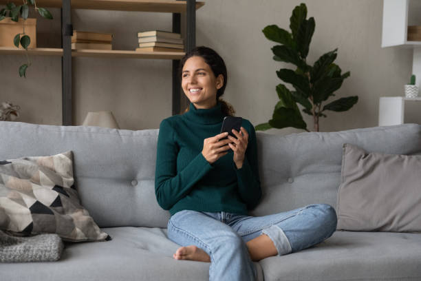 istock Young female sit on sofa look aside distracted from cell 1356225371