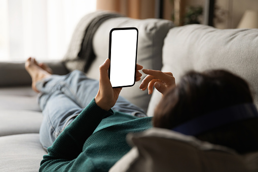 Young woman lying on sofa holding smartphone with empty screen