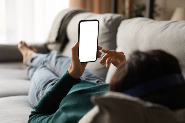 Young woman lying on sofa holding smartphone with empty screen stock photo