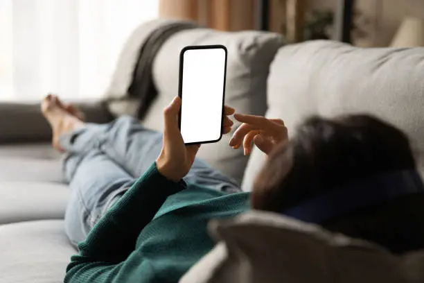 Photo of Young woman lying on sofa holding smartphone with empty screen