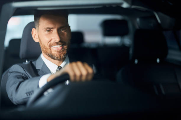 istock Smiling businessman in suit examining auto before purchase 1356227346