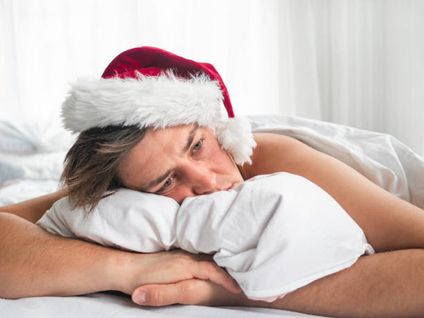 Man in Santa hat is waking up after alco party. He is suffering of headache after New Year or Christmas celebration. Heavy morning. Alcohol withdrawal. Worst hangover. stock photo