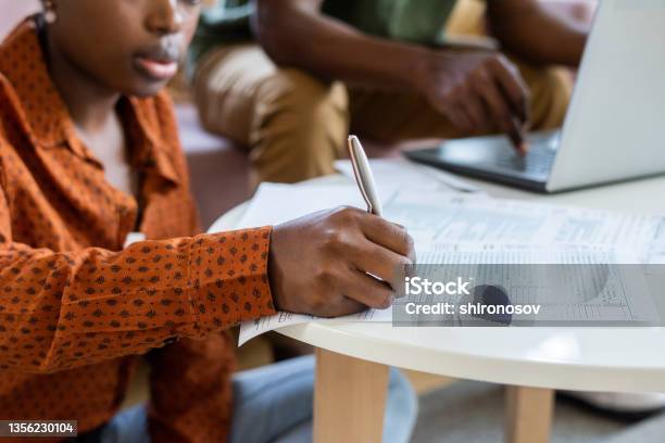 Blackwoman Filling Papers At Coffee Table Stock Photo - Download Image Now - 20-24 Years, 25-29 Years, Adult
