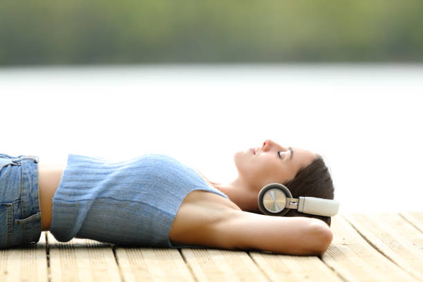 femme détendue écoutant de la musique allongée sur une jetée - lying on side audio photos et images de collection