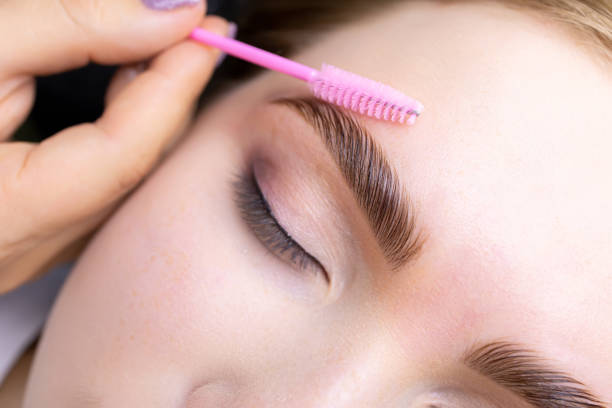 Eyebrow lamination blonde model eyebrow lamination macro photography of the model's hairs the master combs the eyebrow hairs with a pink brush after the procedure long-term styling and lamination forehead photos stock pictures, royalty-free photos & images